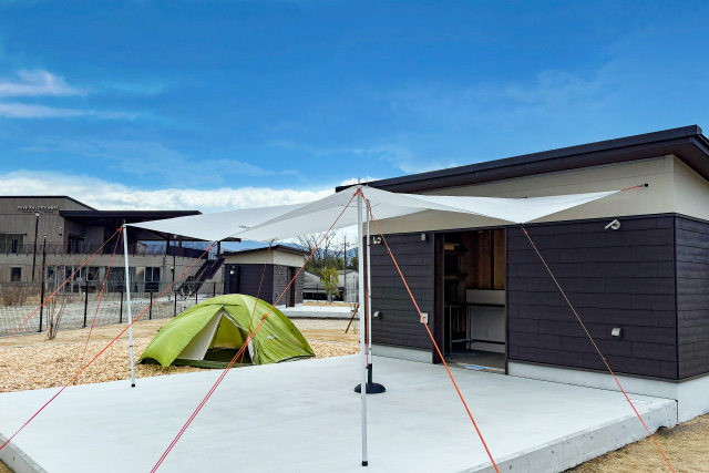 ユニットキャンプサイトの全景画像。ダイニングスペースに専用タープを取り付け、奥のテント設営スペースには緑色のテントが設営されている。