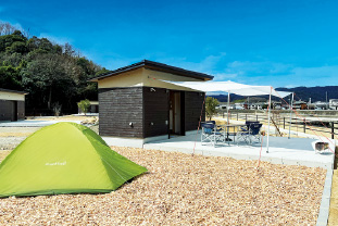 ユニットキャンプサイトをテント設営スペースから撮影した画像。ダイニングスペースに専用タープを取り付け、テント設営スペースには緑色のテントが設営されている。